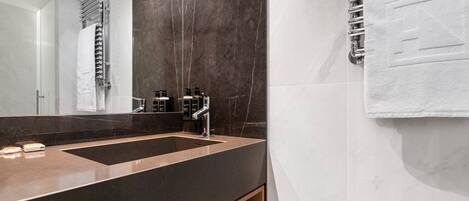 A modern bathroom with a large mirror, dark marble walls, a dual sink vanity, and a towel rack.