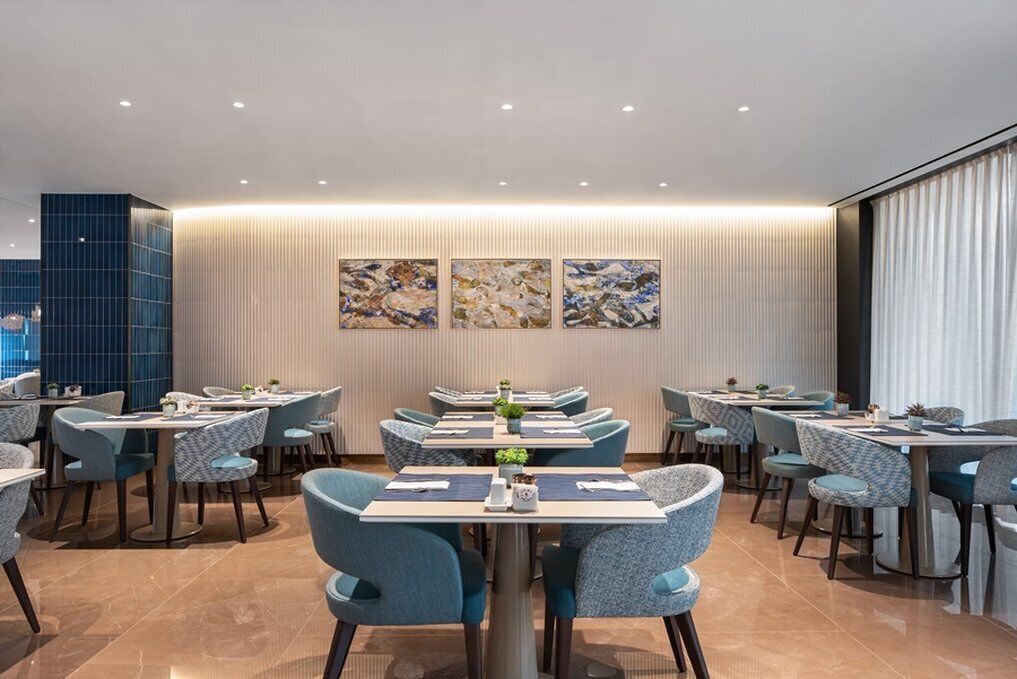 Un comedor moderno con varias mesas y sillas, una pared decorativa con arte abstracto y un ventanal con cortinas.