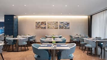 Un comedor moderno con varias mesas y sillas, una pared decorativa con arte abstracto y un ventanal con cortinas.