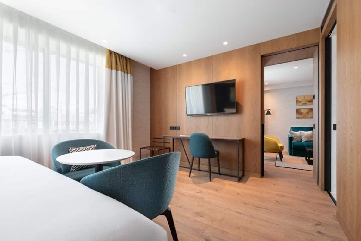 Habitación de hotel moderna con una cama grande, un escritorio, un televisor y vistas a la ciudad.