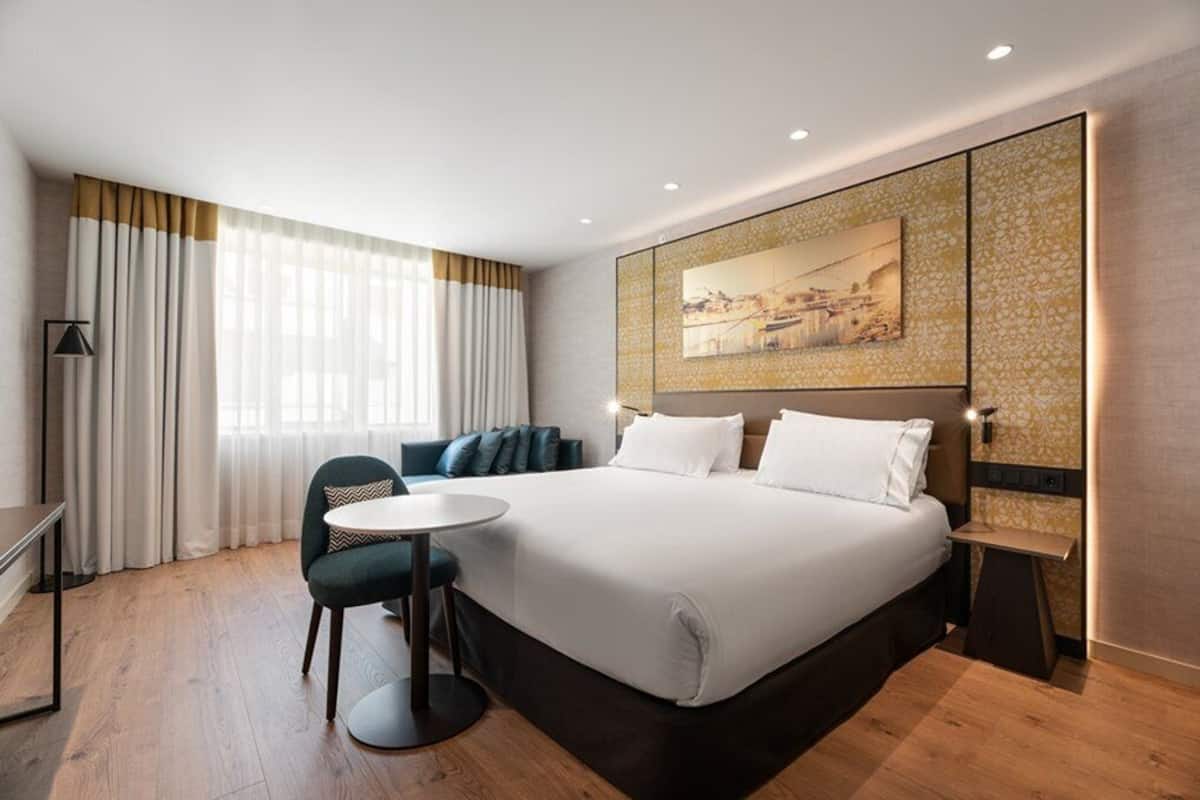 Una habitación de hotel moderna con una cama grande, un escritorio, una silla y una mesita.
