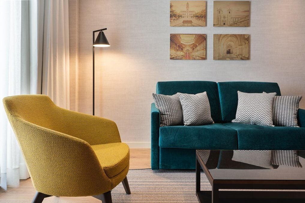 A living room with a teal sofa, mustard armchair, and a floor lamp.