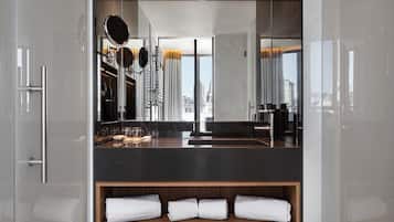 Un baño moderno con cabina de vidrio, tocador con espejo y vistas a la ciudad.