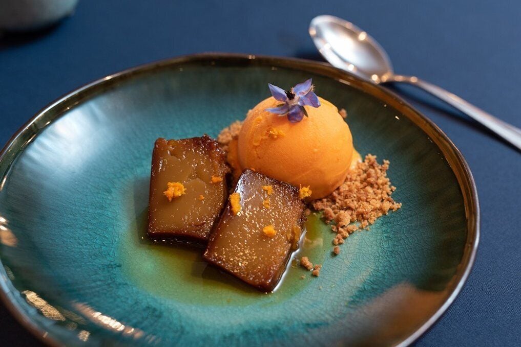 Un piattino con una pallina di gelato, cubetti caramellati e un fiore.