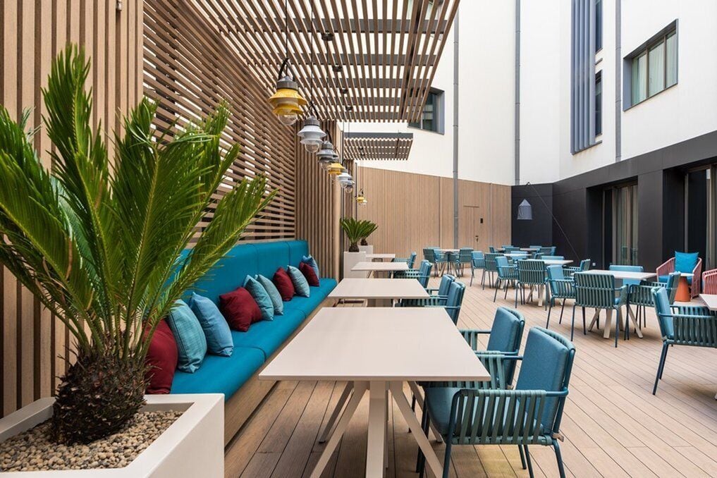 An outdoor seating area with a long blue sofa, multiple tables, and chairs.
