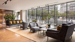 Un lobby moderno con un conjunto de sofás, sillones y una mesa de centro. Hay plantas en macetas y una vista a través de un ventanal grande.