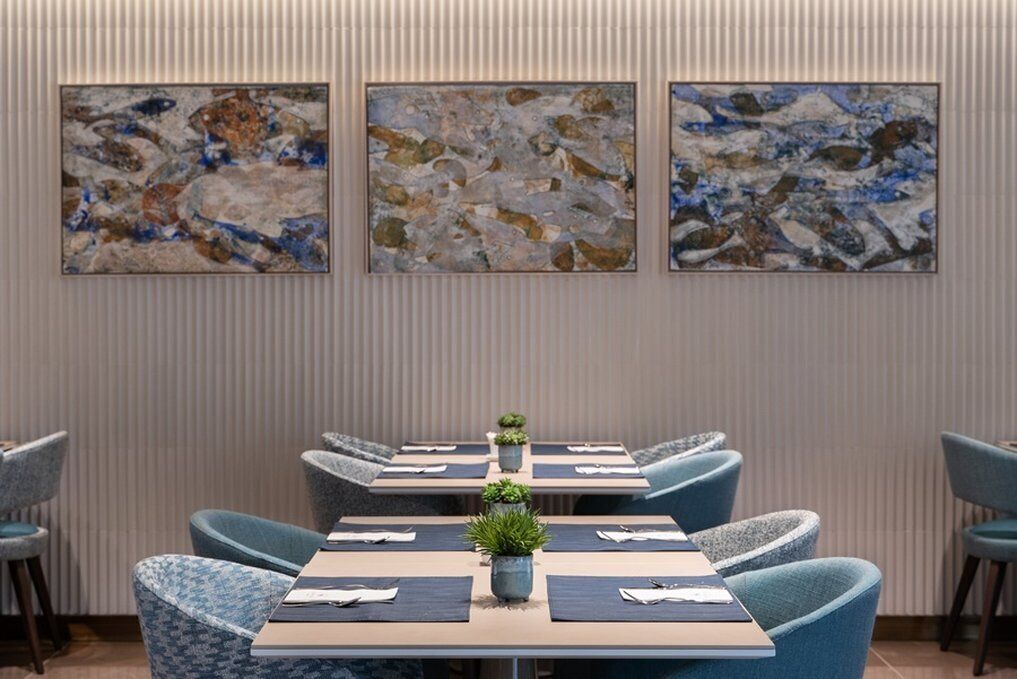 A conference room with a long table, blue upholstered chairs, and abstract paintings on the wall.