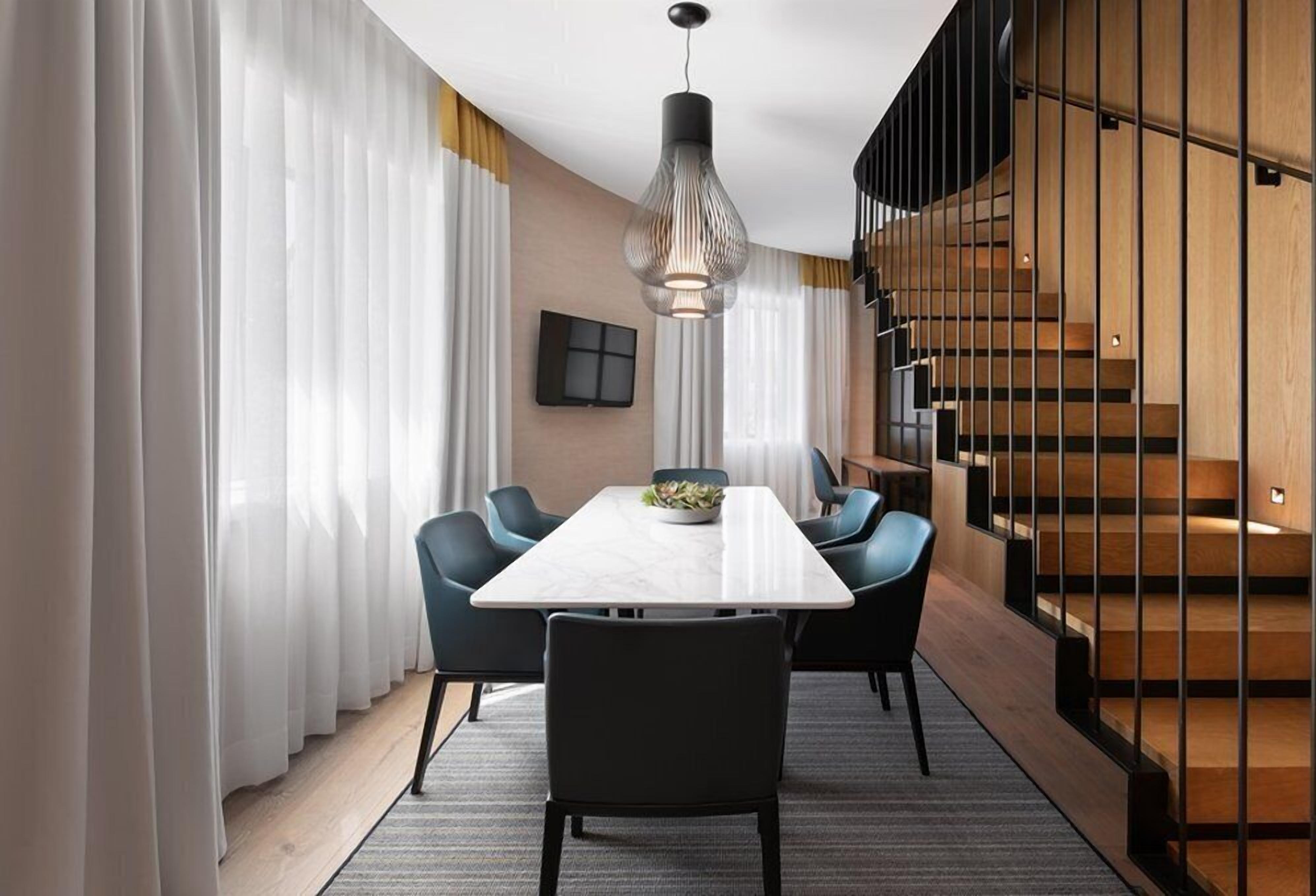 A modern dining area with a long table, chairs, and a hanging light fixture.