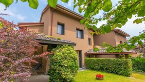 A two-story building with a flat roof, a covered patio area, and a well-maintained garden with a lawn and a flower bed. - Residenza La Parusciola: 3 Beds Duplex With Shared Pool (Gignese)