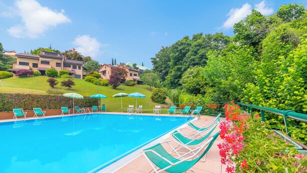 A swimming pool with lounge chairs and umbrellas, surrounded by greenery and a building in the background. - Residenza La Parusciola: 3 Beds Duplex With Shared Pool (Gignese)