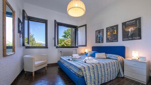 A bedroom with a bed, bedside table, nightstand, chair, and large windows. - Residenza La Parusciola: 3 Beds Duplex With Shared Pool (Gignese)