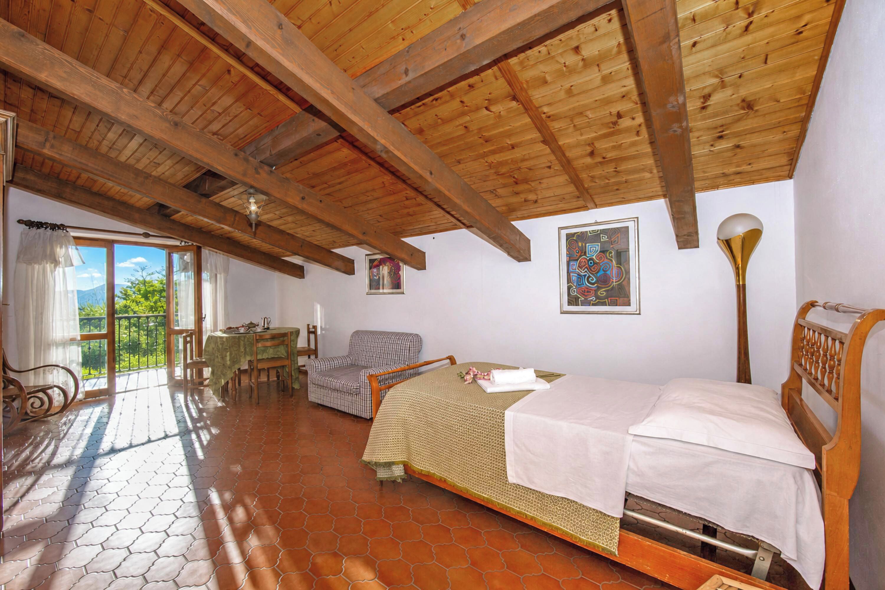 A room with a bed, a chair, a table, and a balcony with a view.