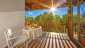 Ein Balkon mit Esstisch, Stuhl und Blick auf Bäume und Himmel.