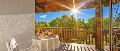 A balcony with a table set for a meal, a chair, and a view of trees and sky.