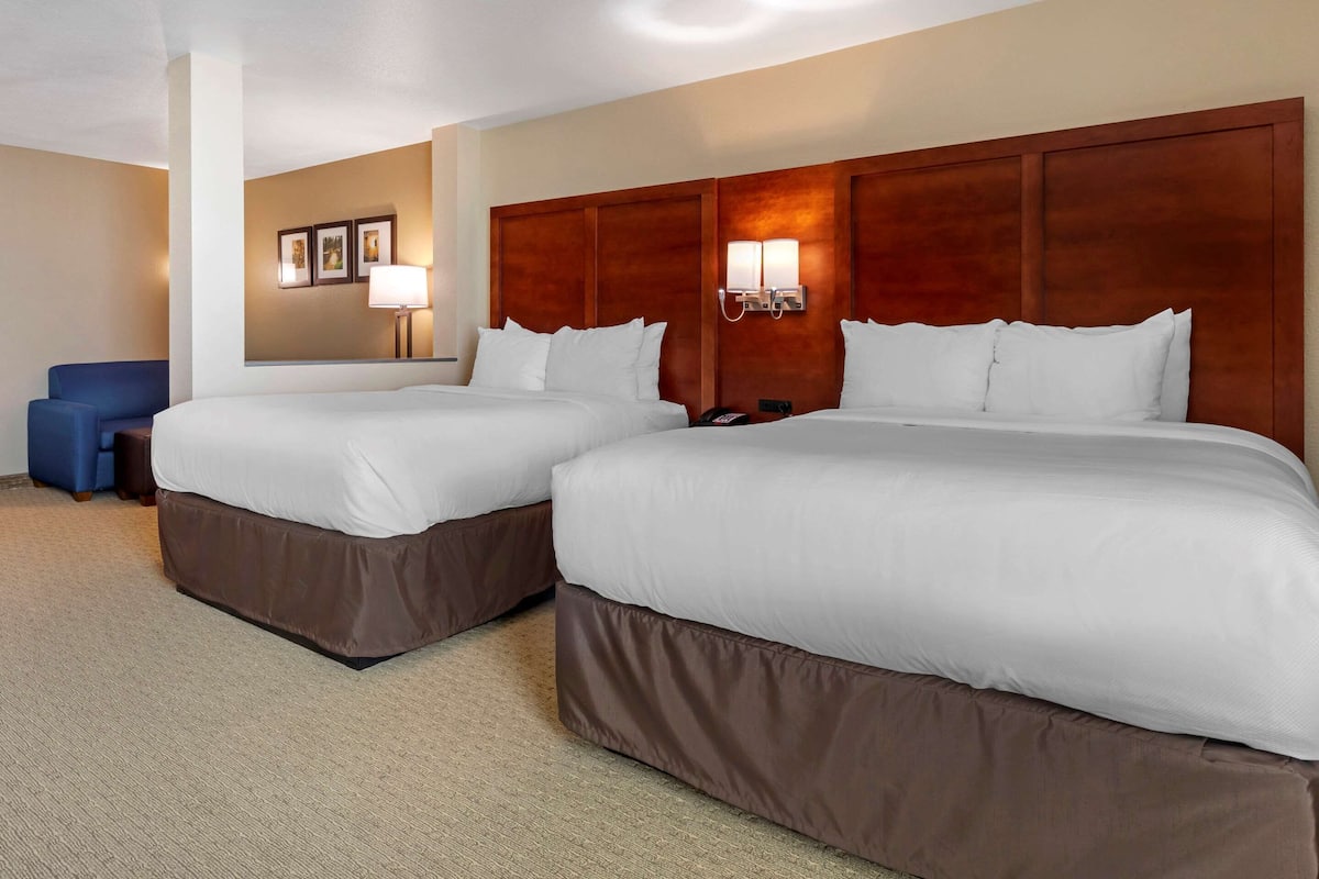 A hotel room with two beds, a blue chair, and a wall-mounted lamp.