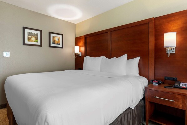 A hotel room with a large bed, wooden headboard, two wall-mounted lights, a bedside table with a phone, and a small drawer.