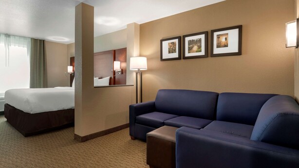 Habitación de hotel con cama, sofá azul, una mesita y tres cuadros en la pared.