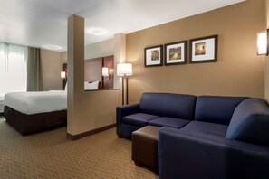 Habitación de hotel con cama, sofá azul, una mesita y tres cuadros en la pared.