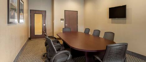 Un salón de conferencias con una mesa grande, seis sillas, una puerta, un televisor y cuadros en la pared.