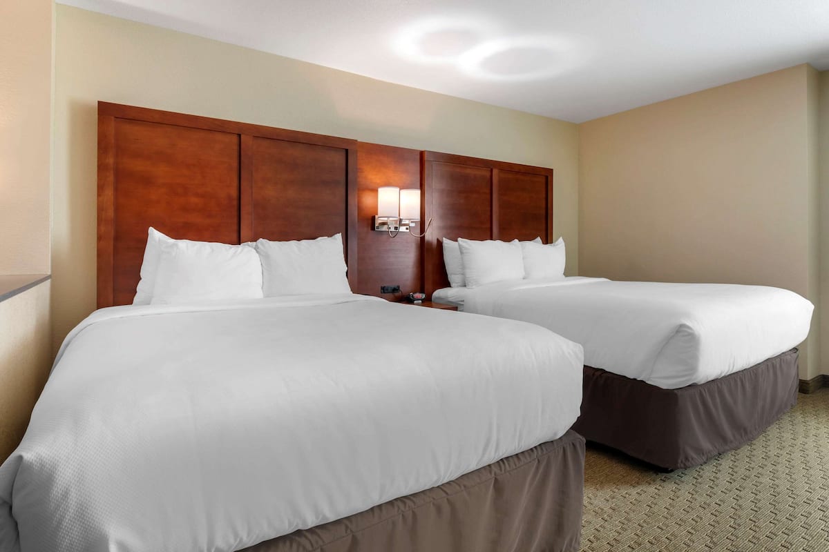 A hotel room with two beds, wooden headboards, and a wall-mounted light fixture.