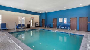 Una piscina interior con paredes azules, agua cristalina y varias sillas azules a su alrededor.