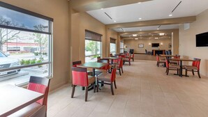Un amplio comedor interior con varias mesas y sillas, ventanas grandes que ofrecen vistas al exterior y un televisor de pantalla plana montado en la pared.