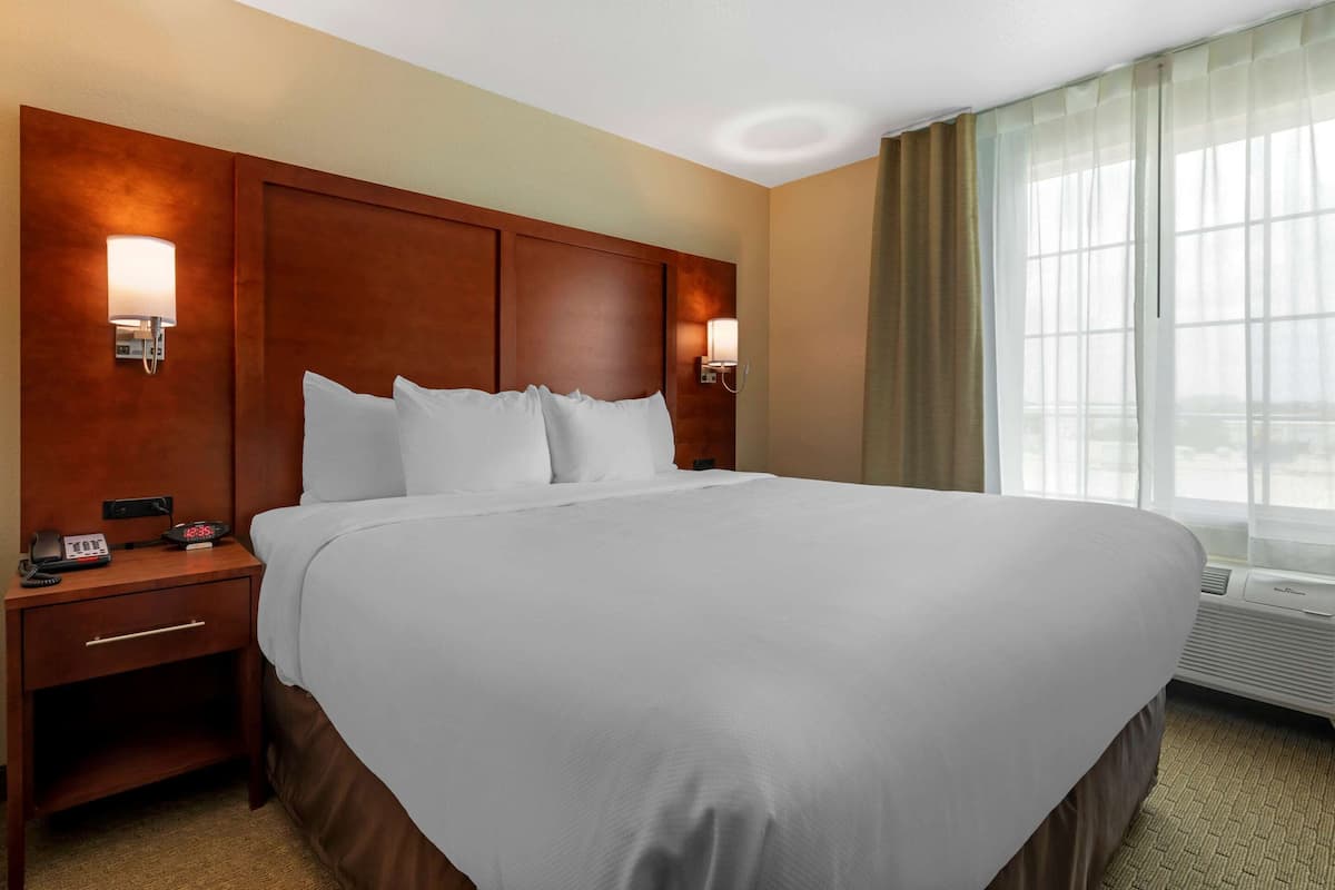 A hotel room with a large bed, wooden headboard, bedside lamps, a nightstand, and a window with curtains.