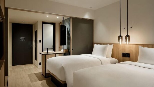 A hotel room with two beds, a desk, a mirror, and a door leading to another room.