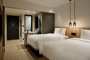 Habitación de hotel con dos camas, un escritorio, un espejo y una puerta que da a otra habitación.
