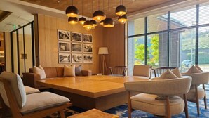 A modern conference room with a large wooden table, comfortable seating, and a large window with a view of the outdoors.
