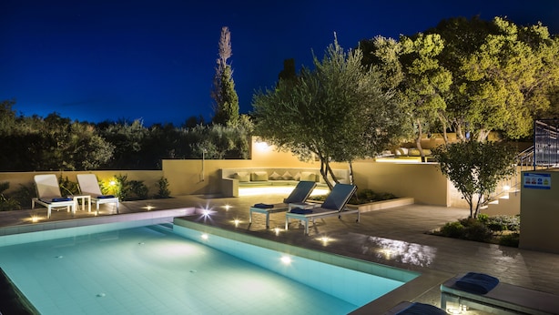Zona de piscina con sillas de descanso y una tumbona, rodeada de árboles y un muro bajo.
