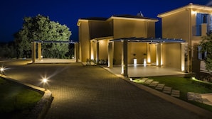 Una casa moderna con entrada pavimentada, iluminación exterior y un patio cubierto.