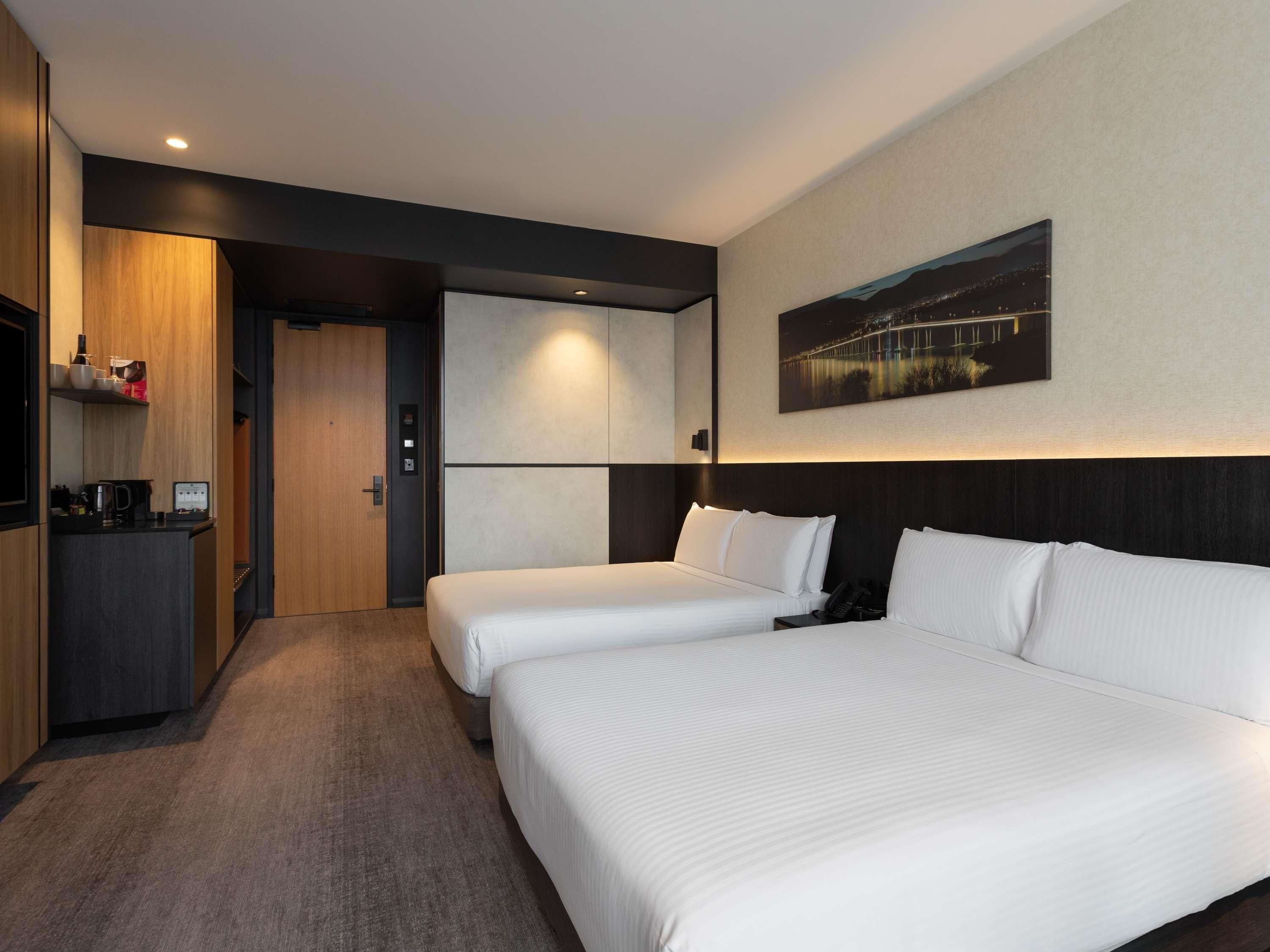 Een hotelkamer met twee bedden, een kitchenette, een badkamer en een stadslandschap schilderij aan de muur.