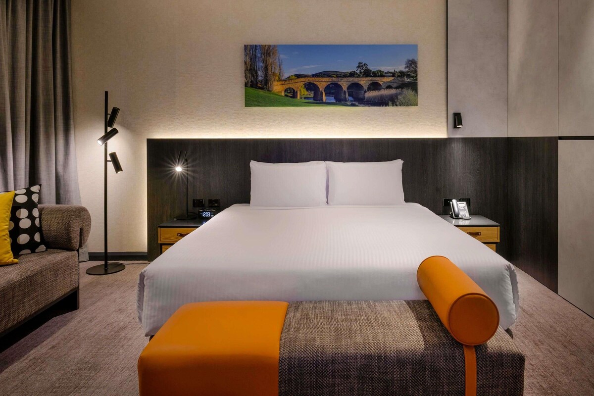 Hotelkamer met een groot bed, een bureau, een stoel, een lamp, een schilderij en een telefoon op het nachtkastje.