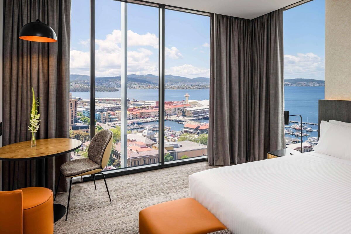 Een hotelkamer met een groot raam, een bed, een ronde tafel en een stoel.