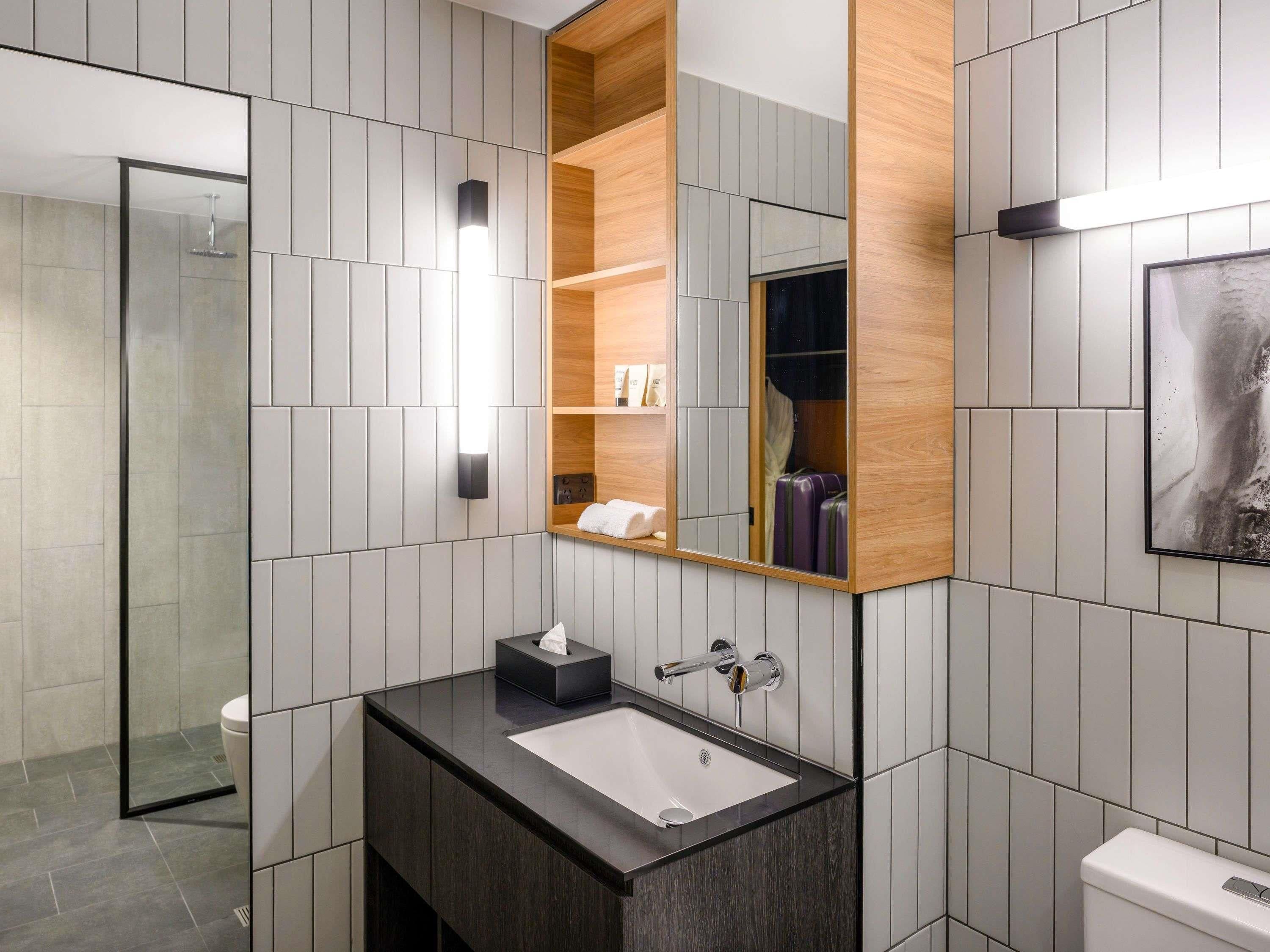 A modern bathroom with a dark countertop sink, a mirror with a wooden frame, and a shower area.