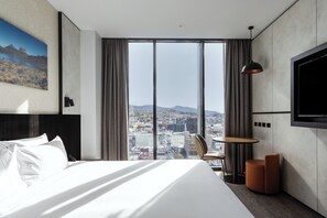 A modern hotel room with a large bed, a round table, a chair, a TV mounted on the wall, and a city view through large windows. - Mövenpick Hotel Hobart (Hobart)