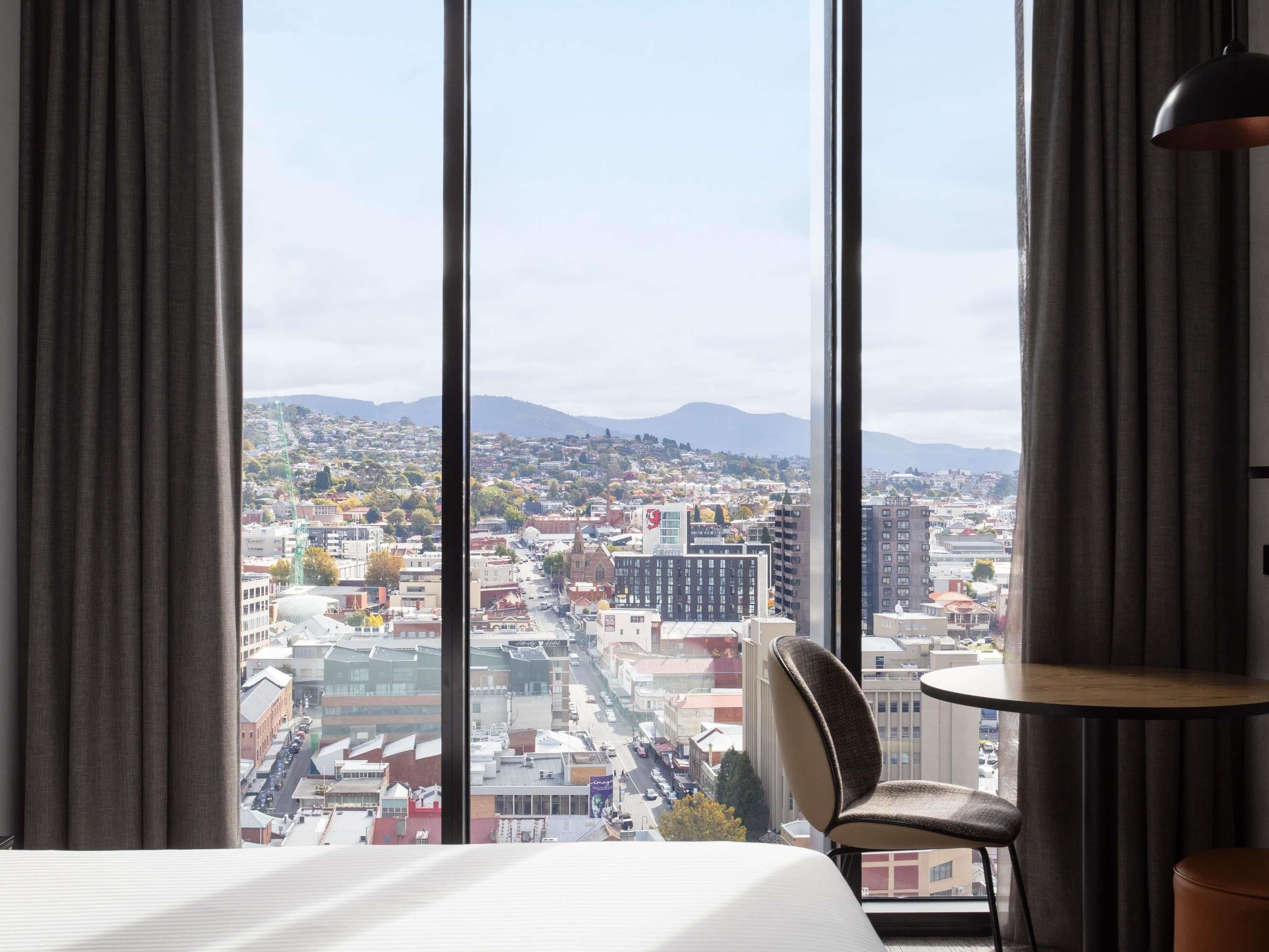 A hotel room with a large window offering a city view.