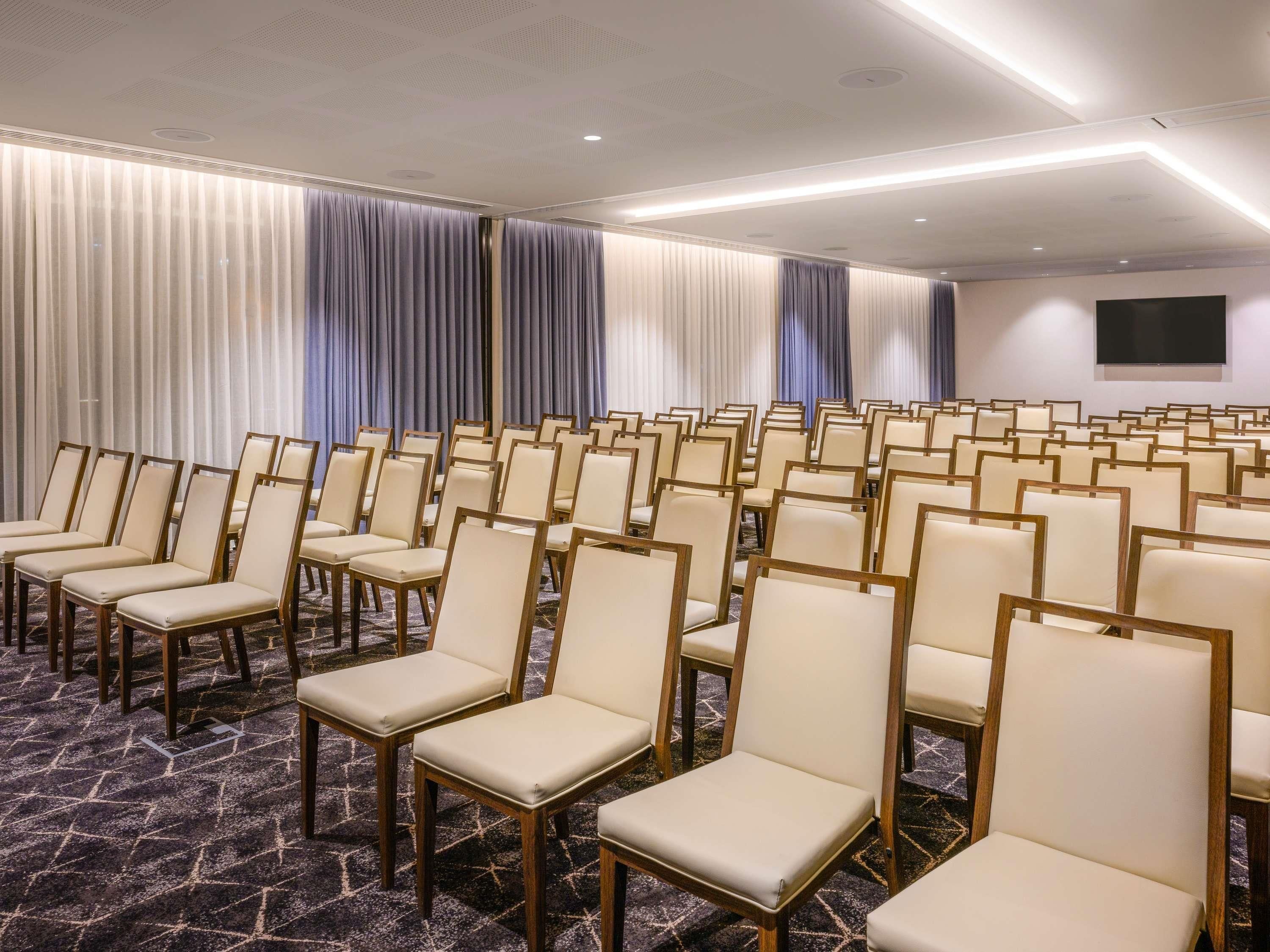 A conference room with rows of chairs, a carpeted floor, and curtains.