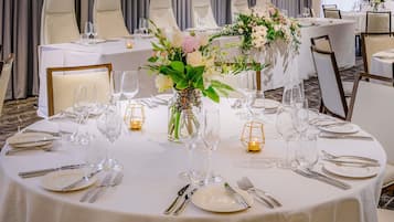 A banquet hall with round tables set for dining, each with white tablecloths, silverware, and glassware.