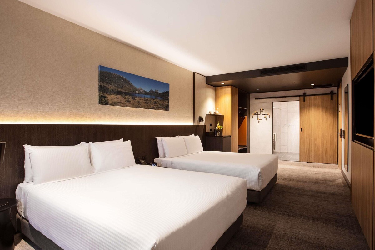 Een hotelkamer met twee bedden, een groot wanddecor, een bureau met lamp en een kledingkast.