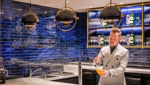 A bar area with a bartender, blue-tiled backsplash, and a shelf with glasses and bottles.