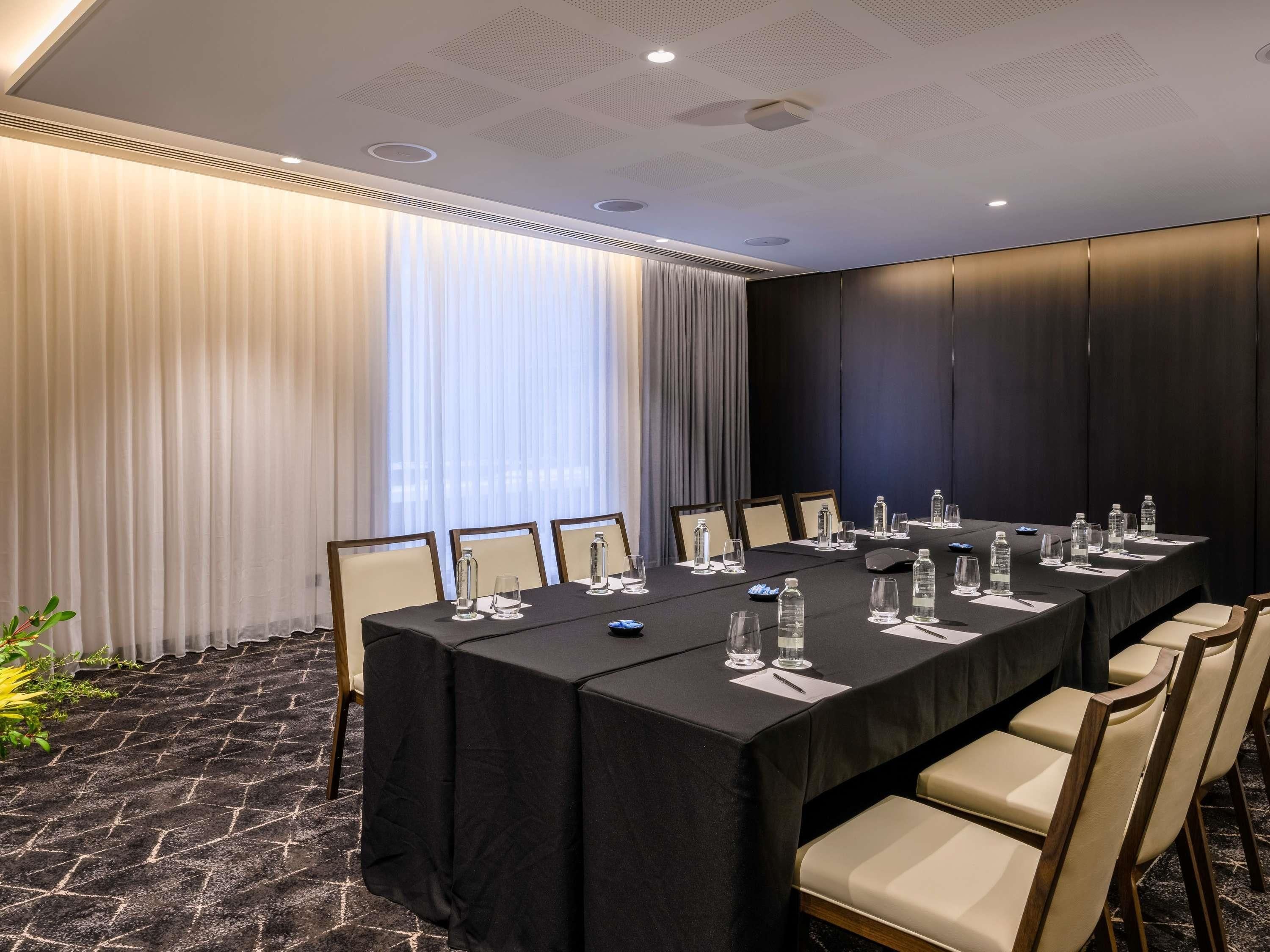 A conference room with a long table, chairs, water bottles, and a plant.