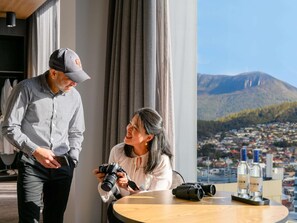 Een man en een vrouw in een kamer met een groot raam dat uitkijkt over een stad en bergen.