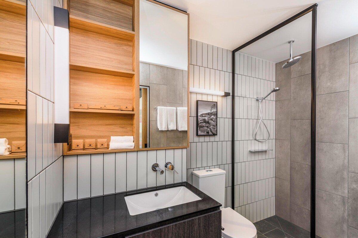 Un baño moderno con lavamanos negro, inodoro blanco y ducha con cerramiento de vidrio.