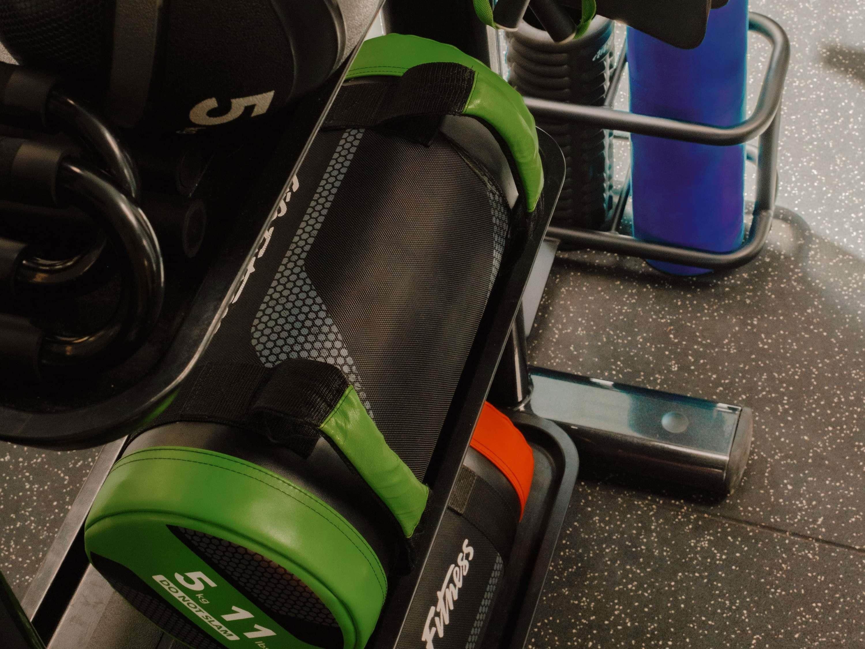 A weightlifting bench with a green weight plate, a black and orange weightlifting belt, and a water bottle on the floor.