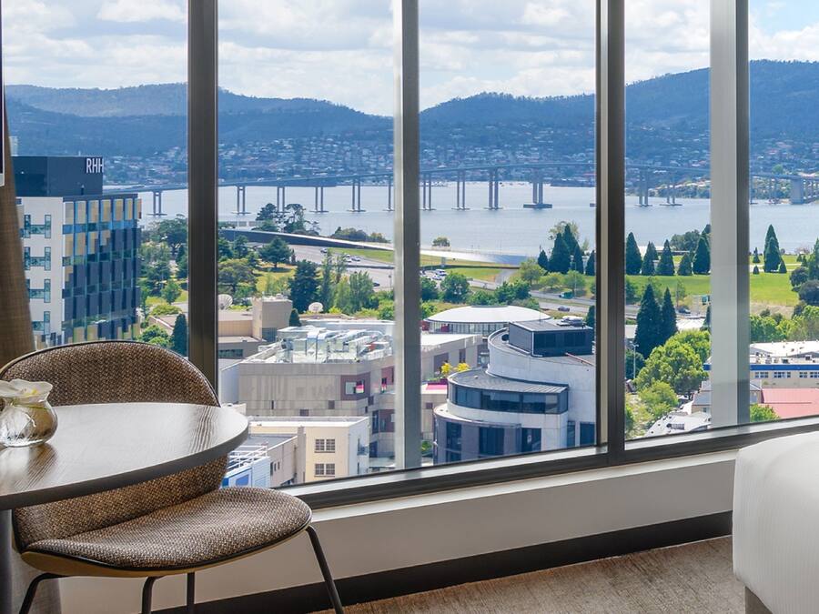 Quarto com uma janela ampla com vista para um horizonte urbano, incluindo uma ponte e colinas.