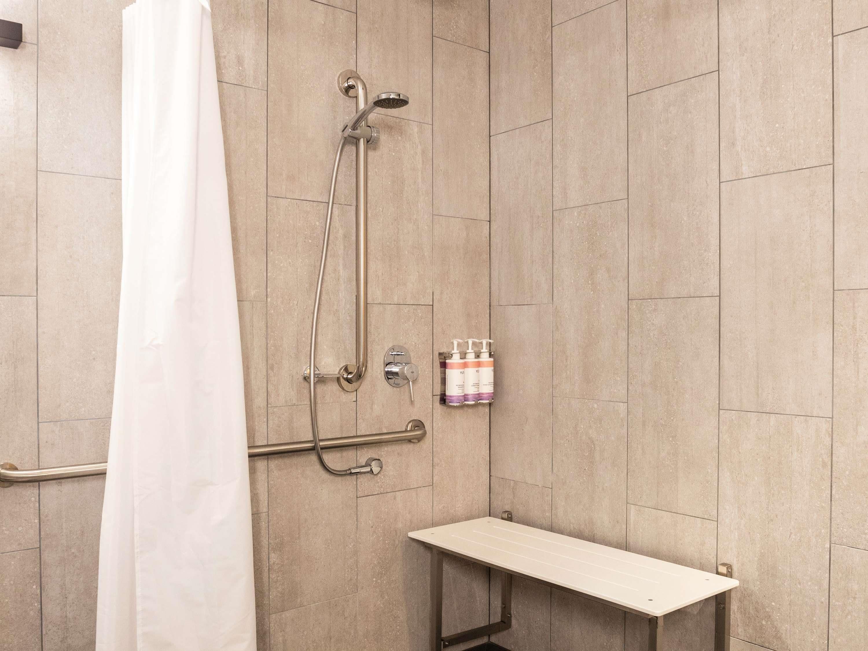Zona de ducha con cabezal de ducha de mano, grifo empotrado en la pared y un pequeño estante con artículos de aseo.