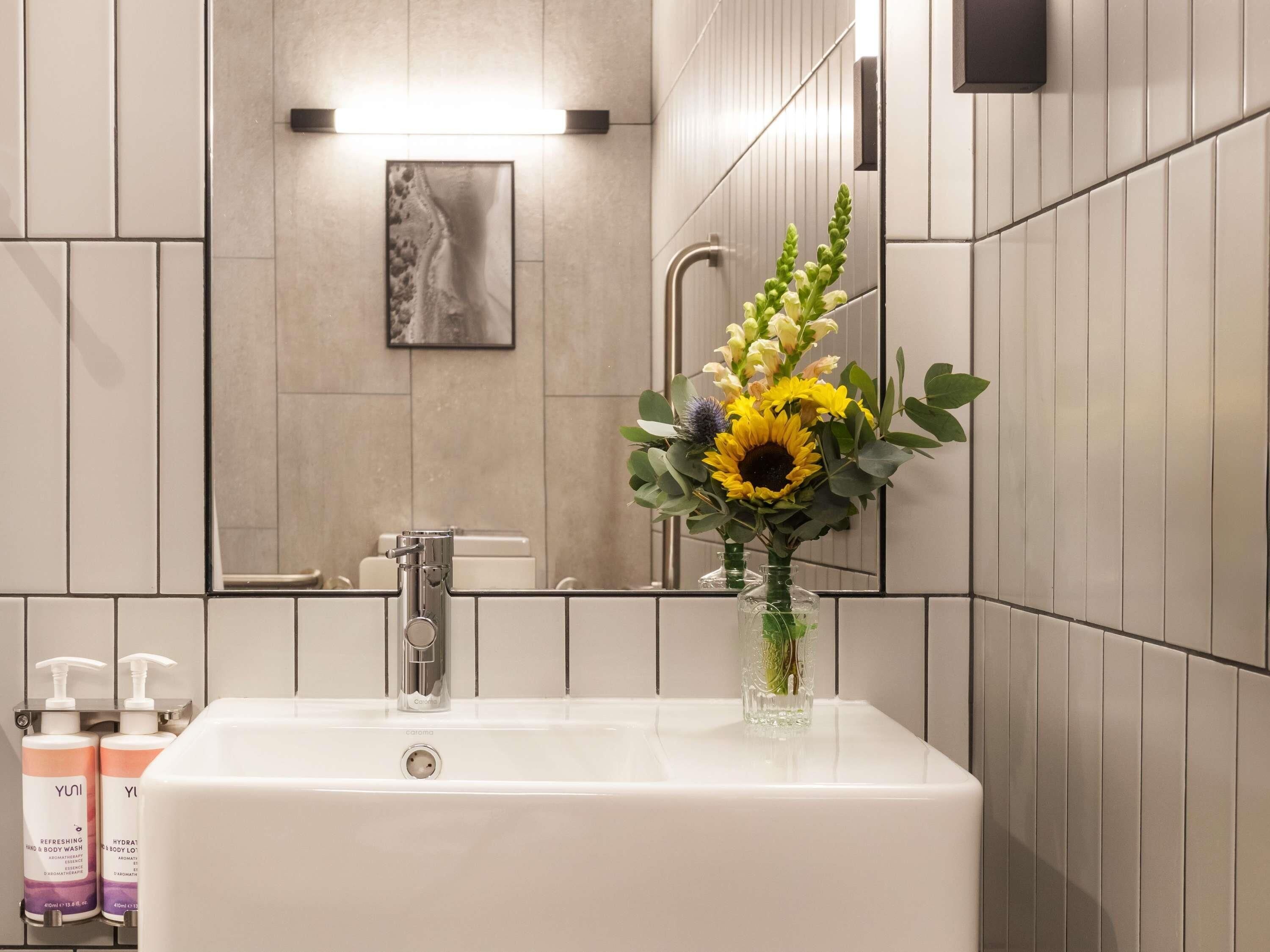 A bathroom with a white sink, a mirror, and a vase with flowers.