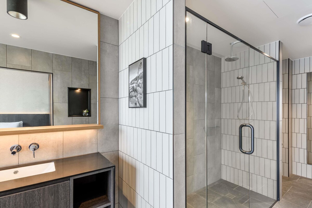 Un baño moderno con un espejo grande, cabina de ducha y tocador con lavamanos y mueble.